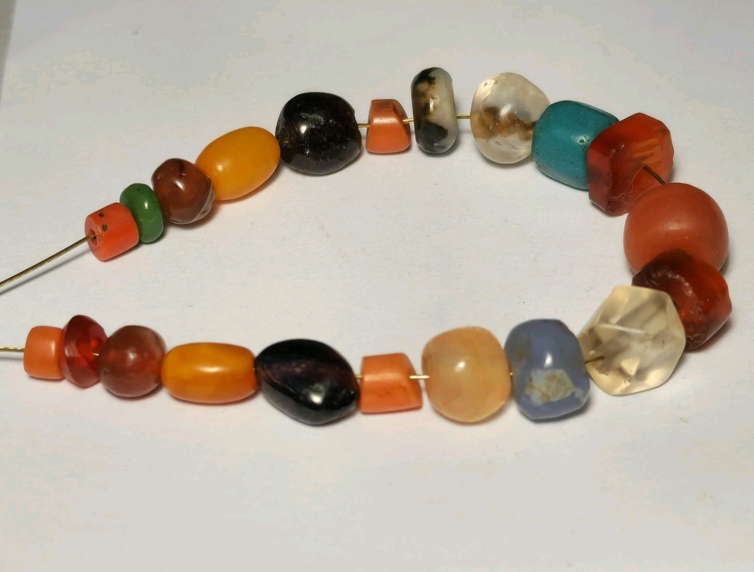 A STRAND OF 21 ANCIENT & ANTIQUE AGATE, GARNET, ROCK CRYSTAL, AMBER, CORAL BEADS