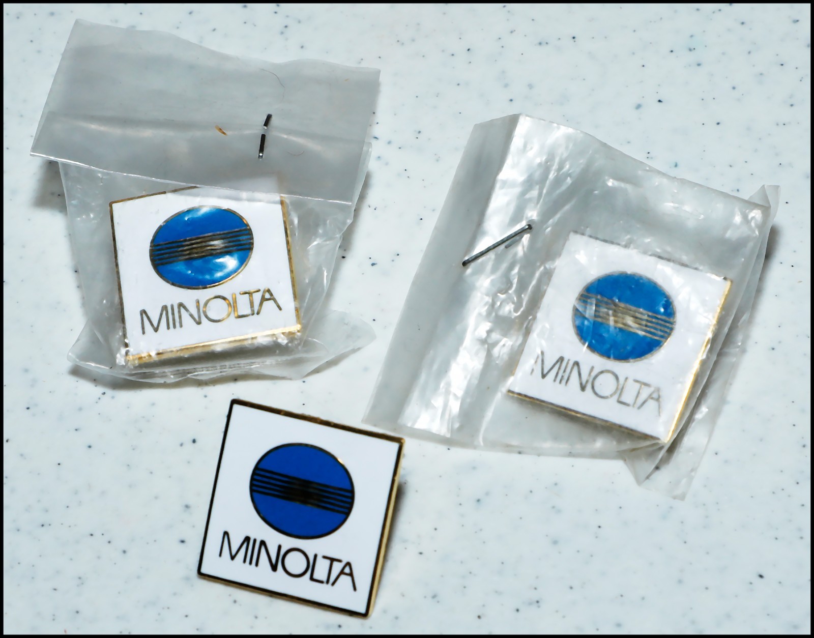 Metal Minolta lapel pin with "Rising Sun" logo on a white background w/ clasp