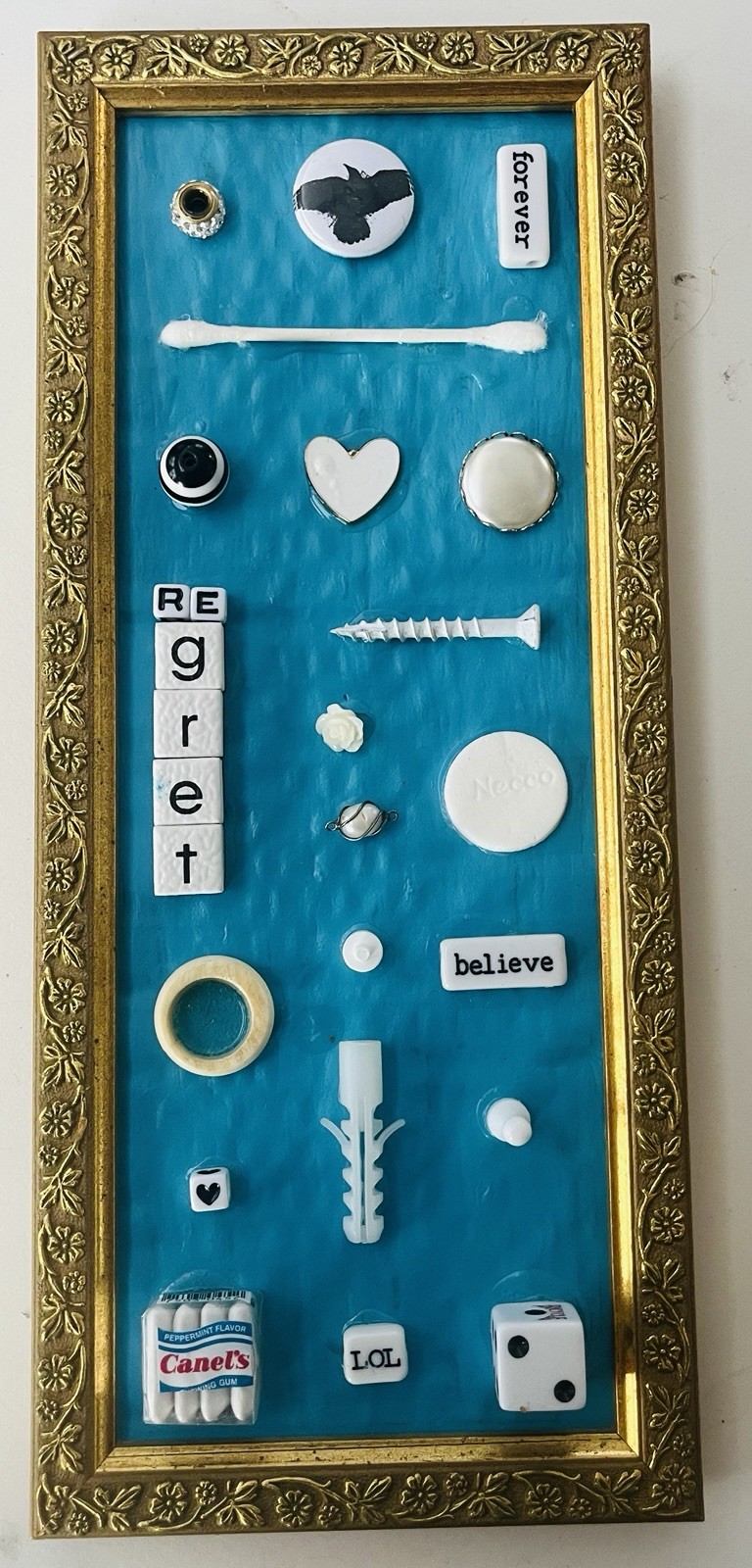 Original art: found white objects on teal background in gold frame. 11” x 5”